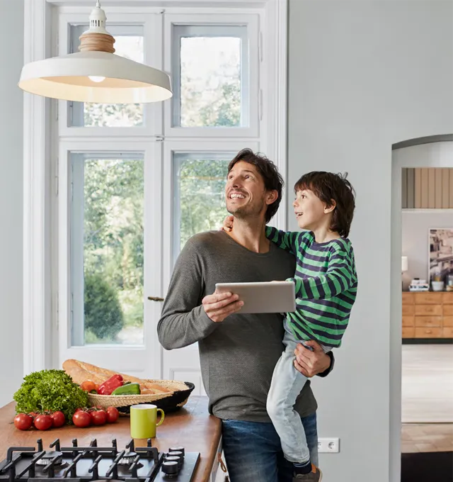 Adult and child in the kitchen.  The man is holding the child and they are both looking up at the light shade.